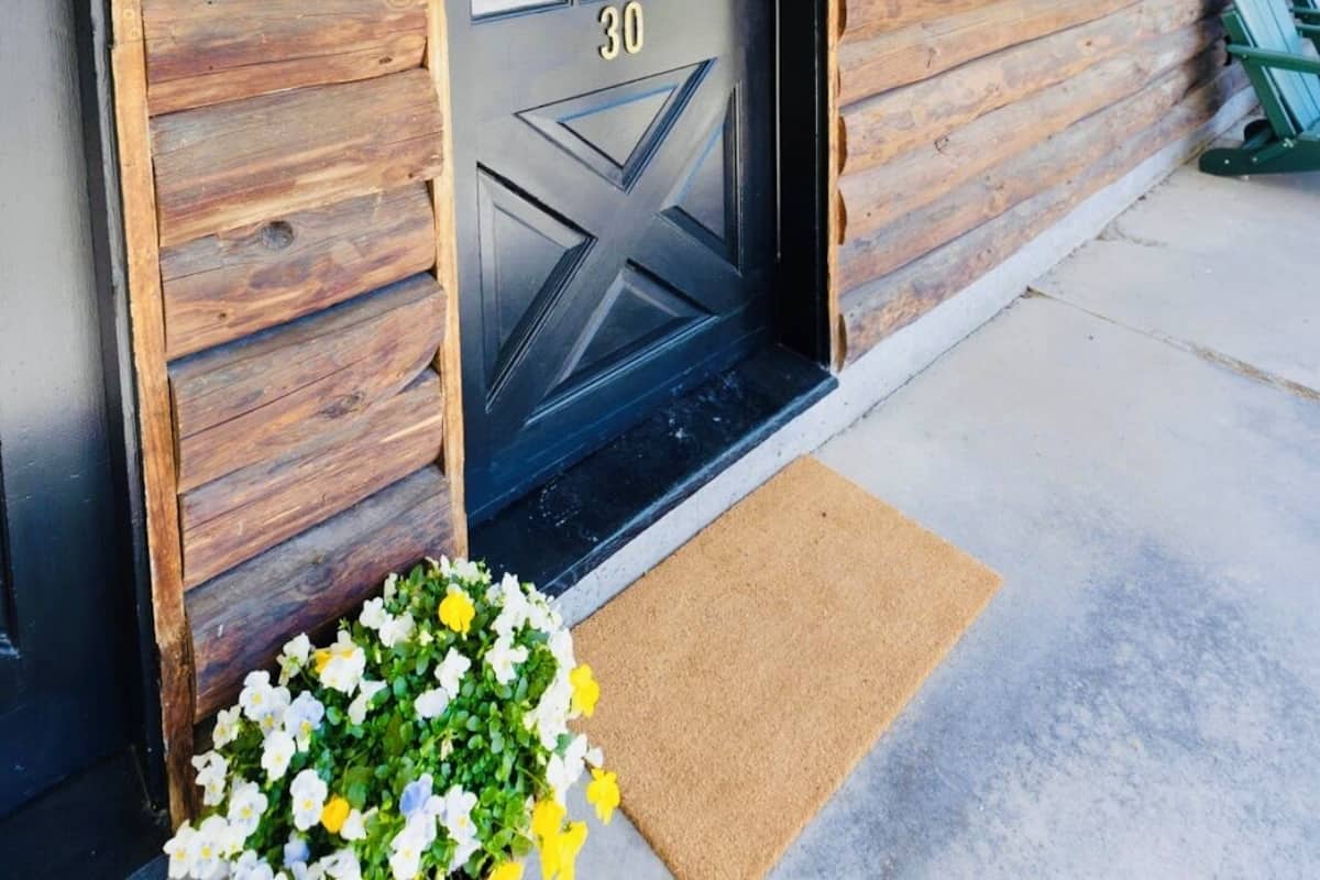 A wooden log cabin with a black door marked with the number 30, a small porch, and a flower arrangement.