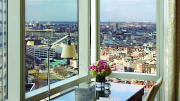 A high-rise room with a city view, a desk with a lamp, and a chair.