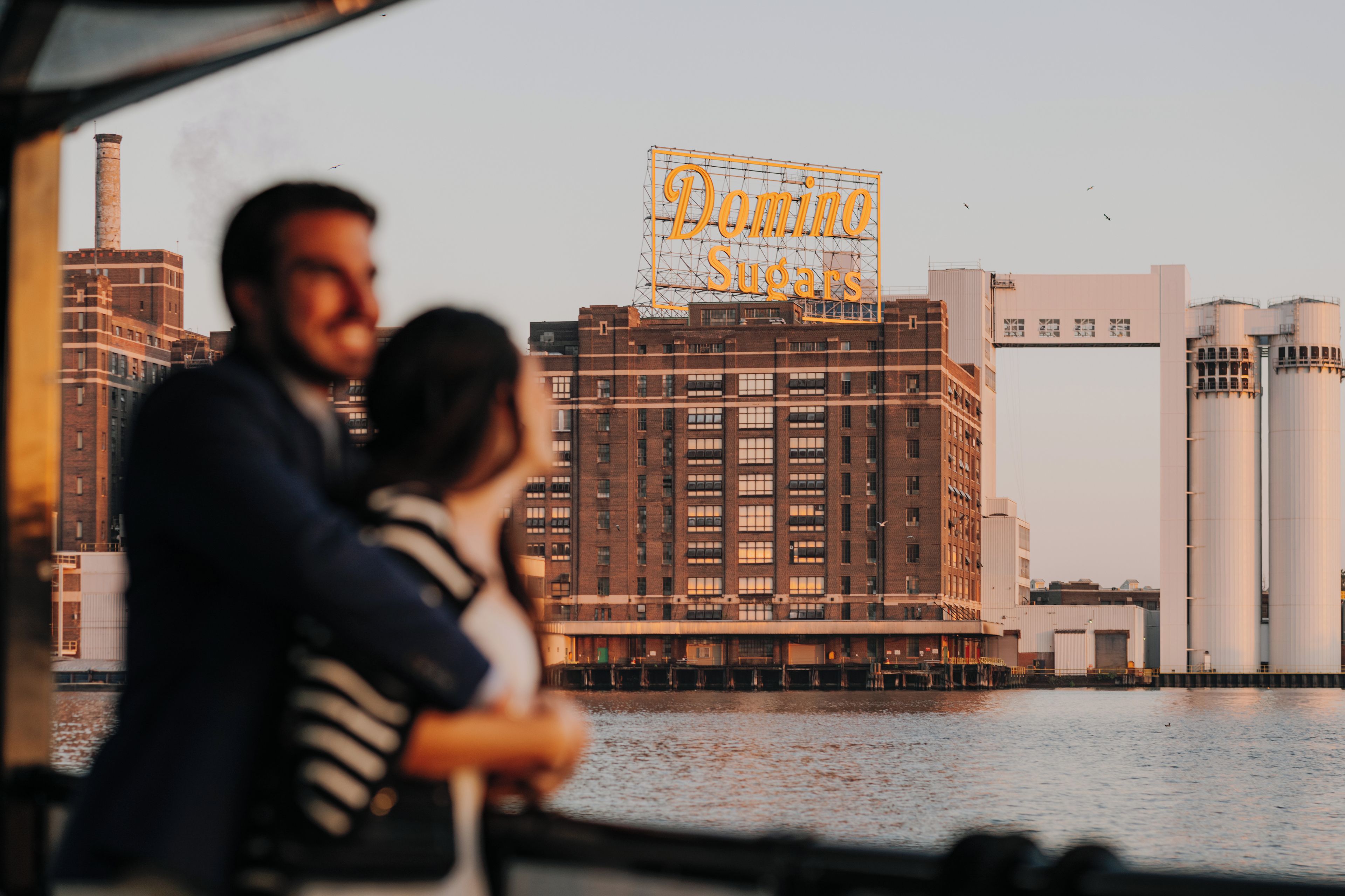 Ett par står och blickar ut över en stadsbild med industriella byggnader och en tydlig skylt med texten ”Domino Sugars”.
