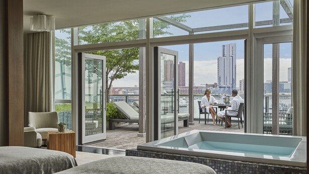 A modern hotel room with a large window, a balcony with a view of the city, a bathtub, and two beds. - Four Seasons Hotel Baltimore (Baltimore)