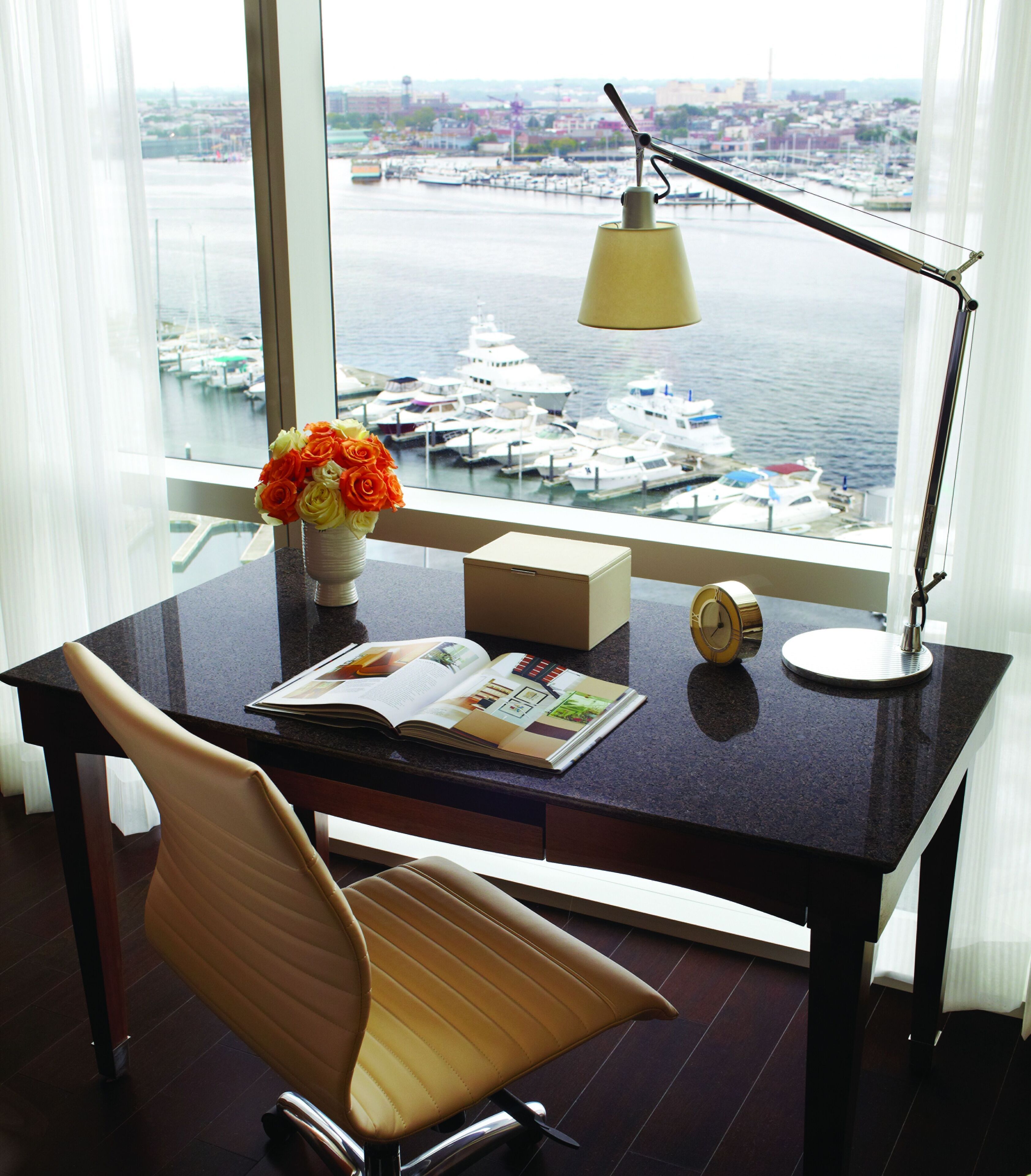 A desk with a book, a vase with flowers, a lamp, and a clock.