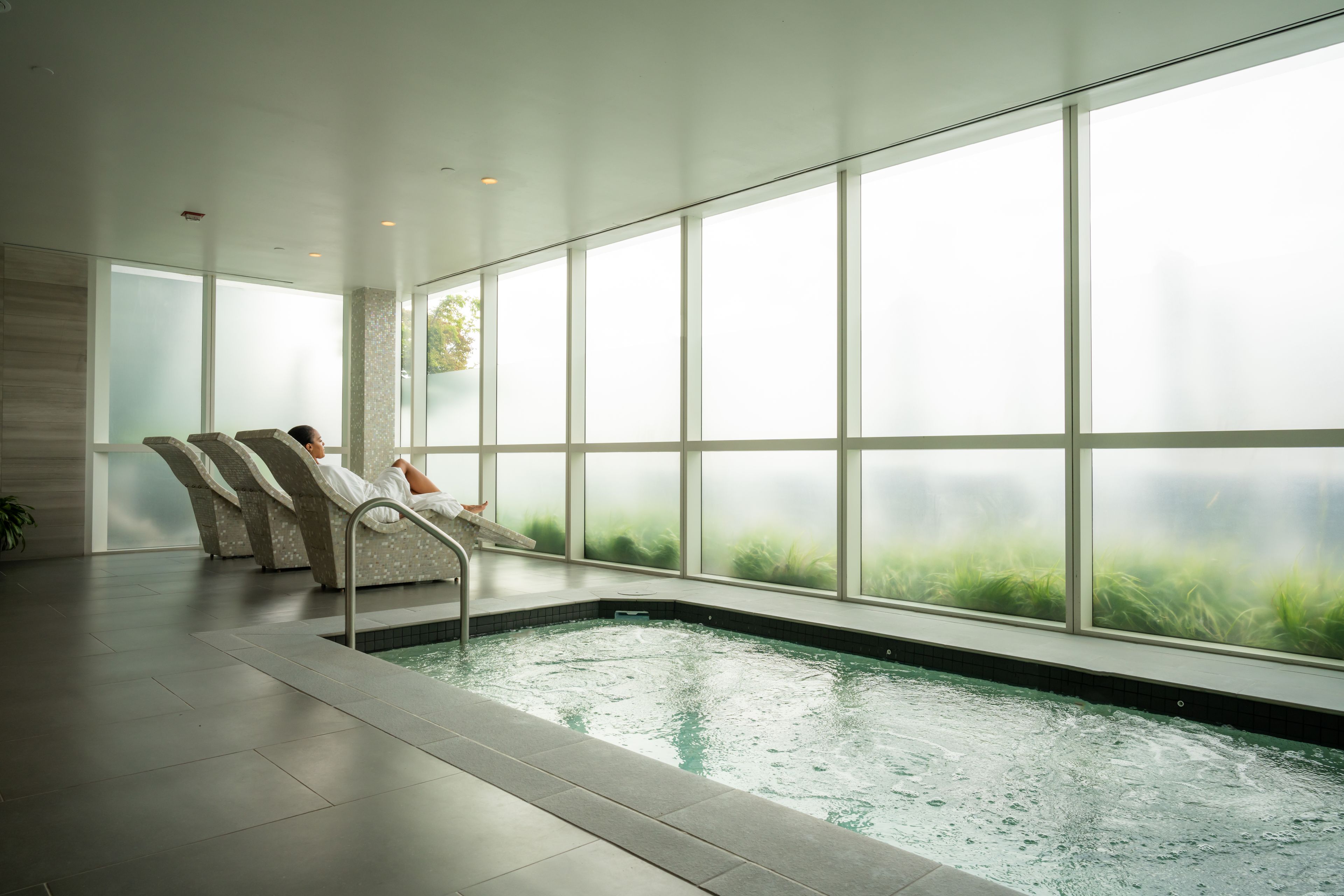 Un área de spa con una amplia piscina interior, zonas de estar y grandes ventanales.