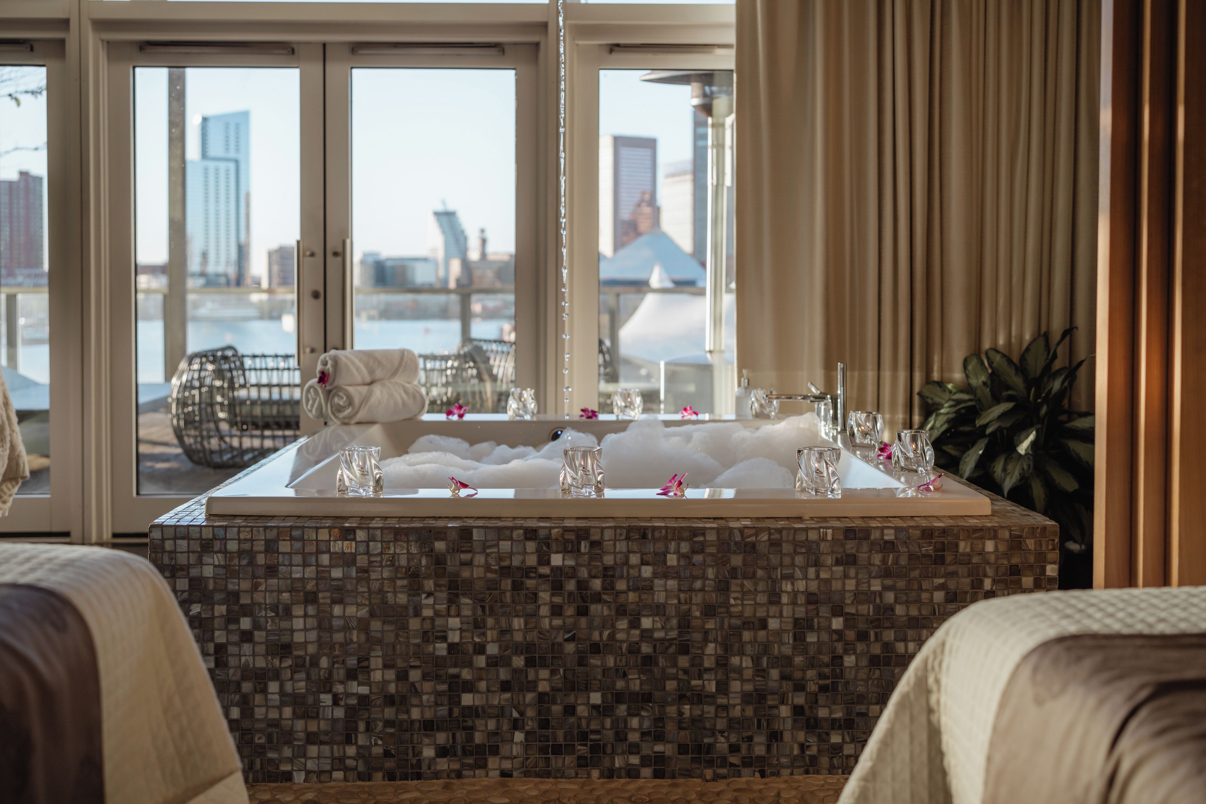 A hotel bathroom with a large bathtub, a glass shower enclosure, and a view of the cityscape through the windows.