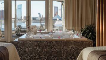 A hotel bathroom with a large bathtub, a glass shower enclosure, and a view of the cityscape through the windows.