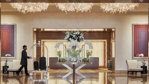 Un hall d’hôtel doté d’un sol réfléchissant, d’un comptoir d’accueil et d’une grande composition florale.