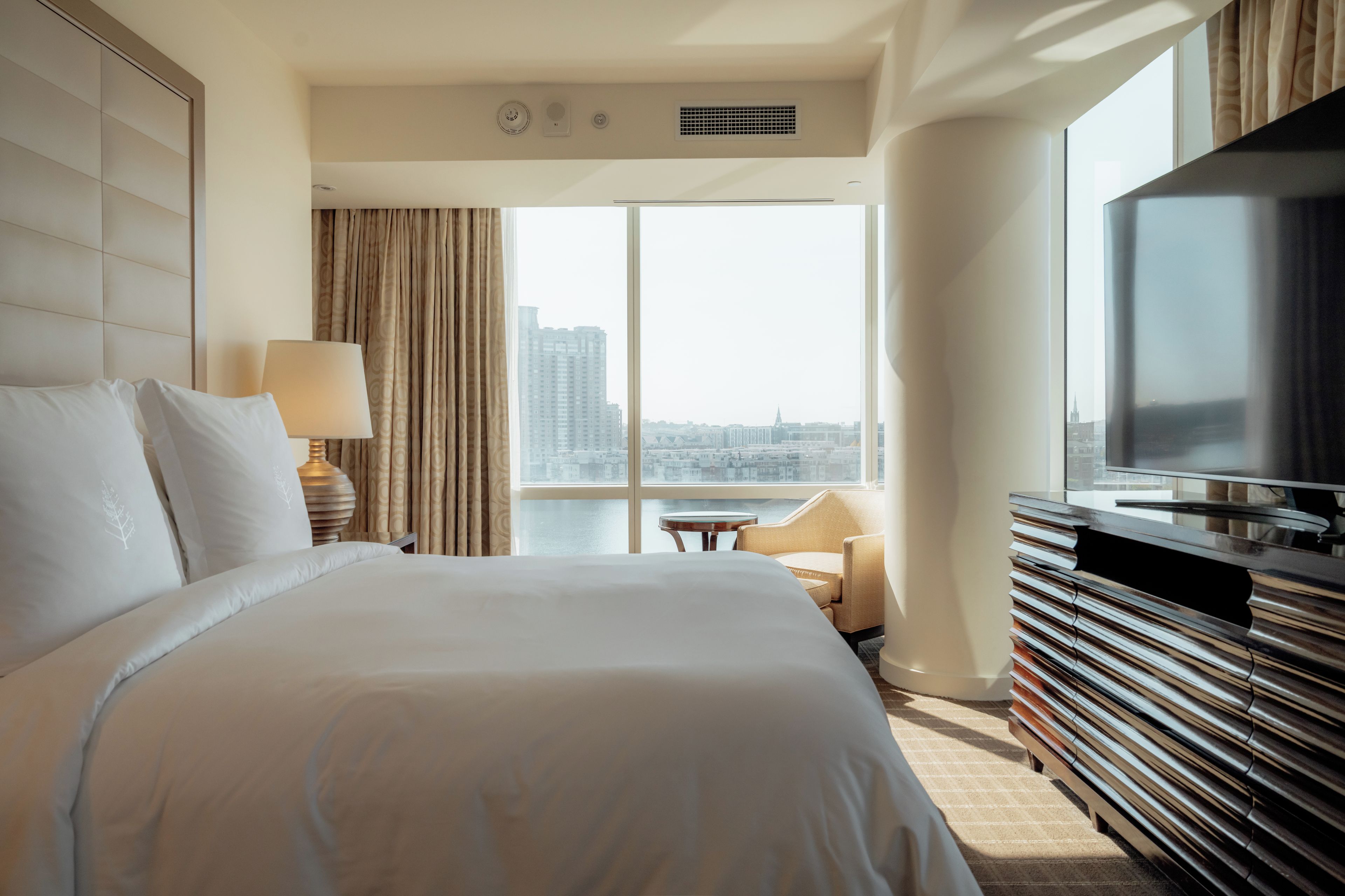 A hotel room with a large bed, a television, a desk, and a view of the cityscape.