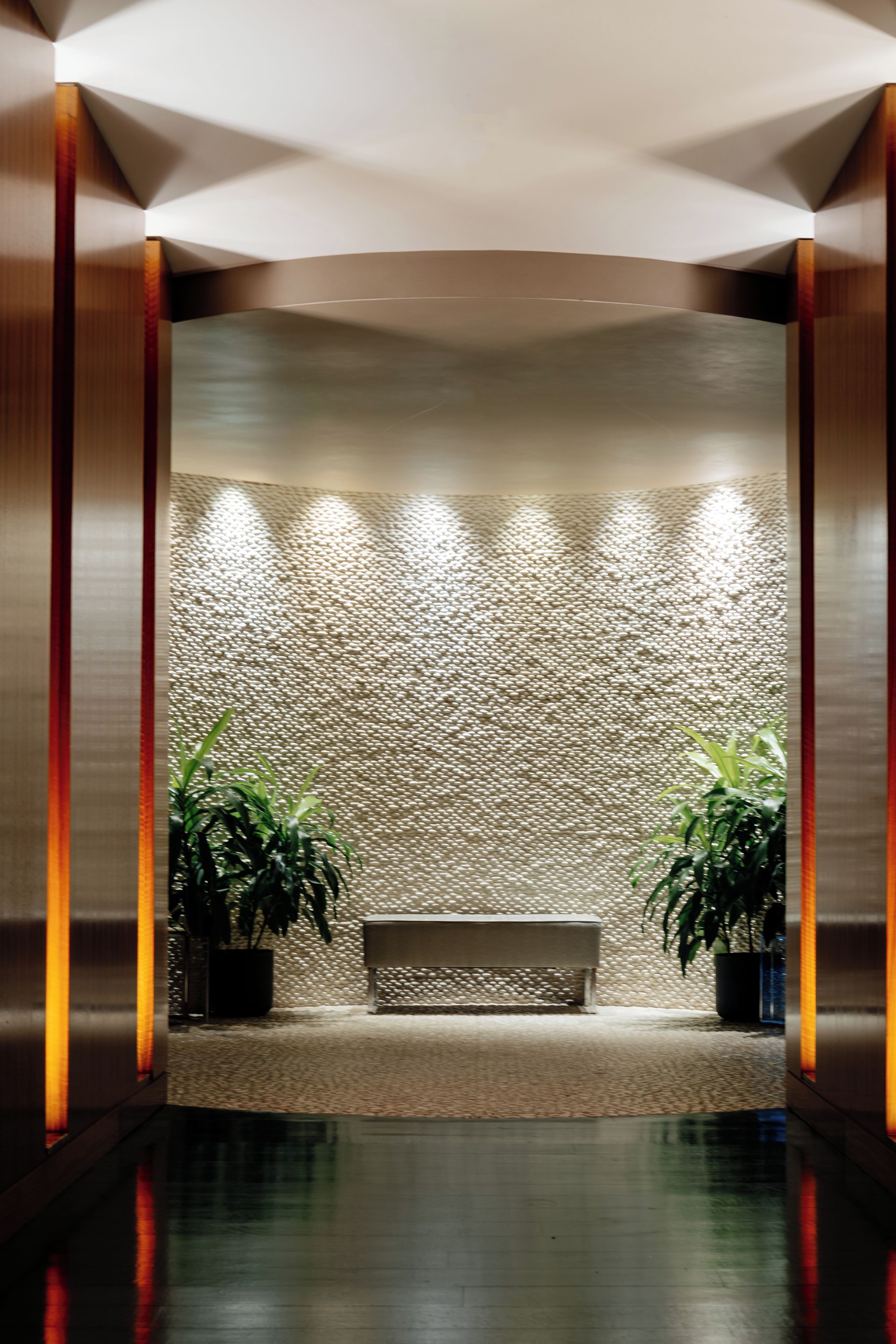 A reception area with a bench, two potted plants, and a textured wall.
