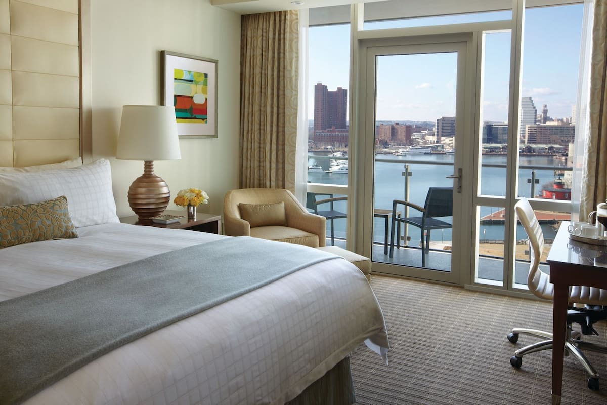 A hotel room with a large bed, a desk, a chair, and a view of a cityscape and water.