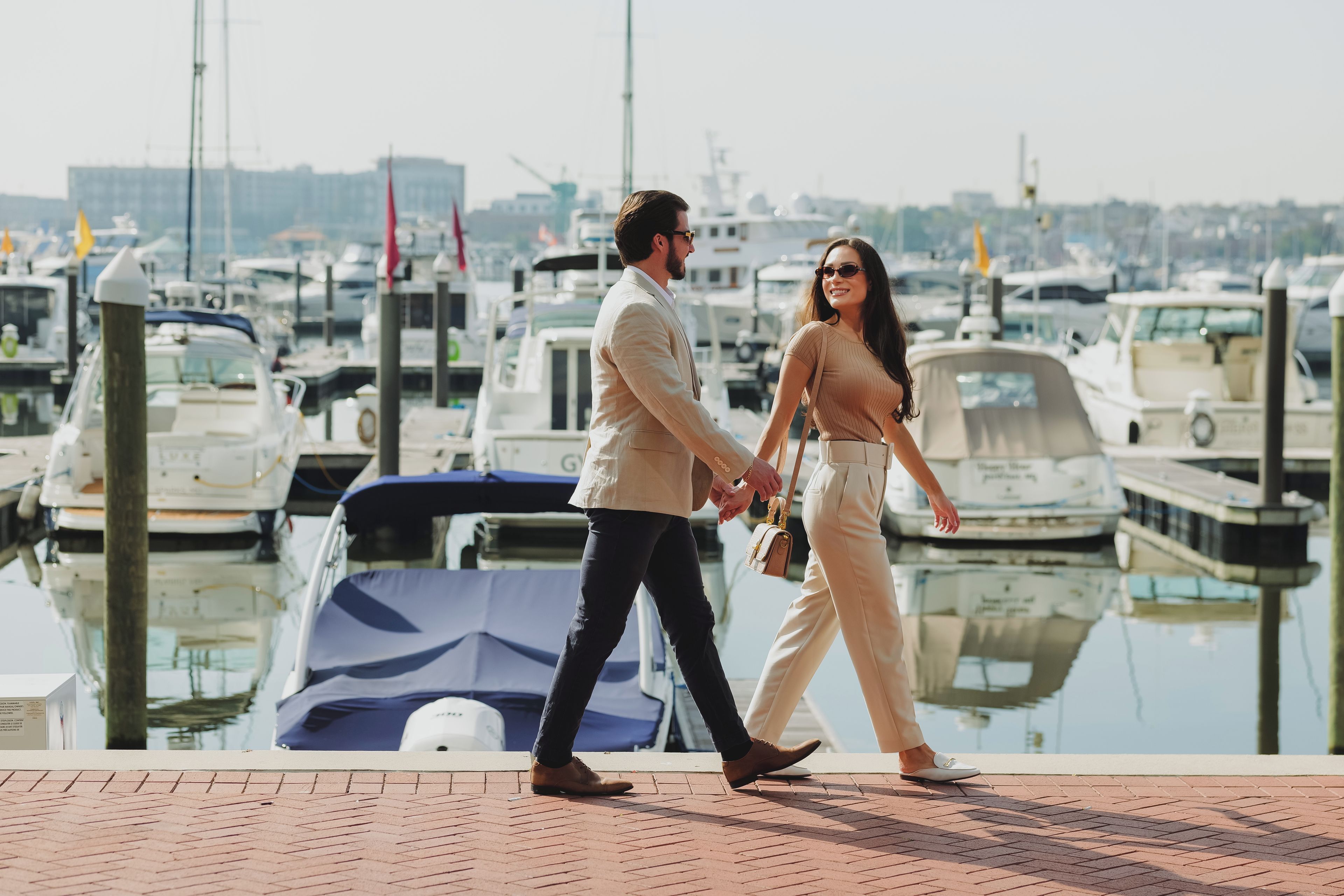 Um casal caminhando em um cais, com barcos ao fundo.