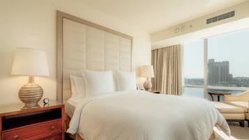 A hotel room with a large bed, two bedside tables, a nightstand, a view of the city, and a window with curtains.