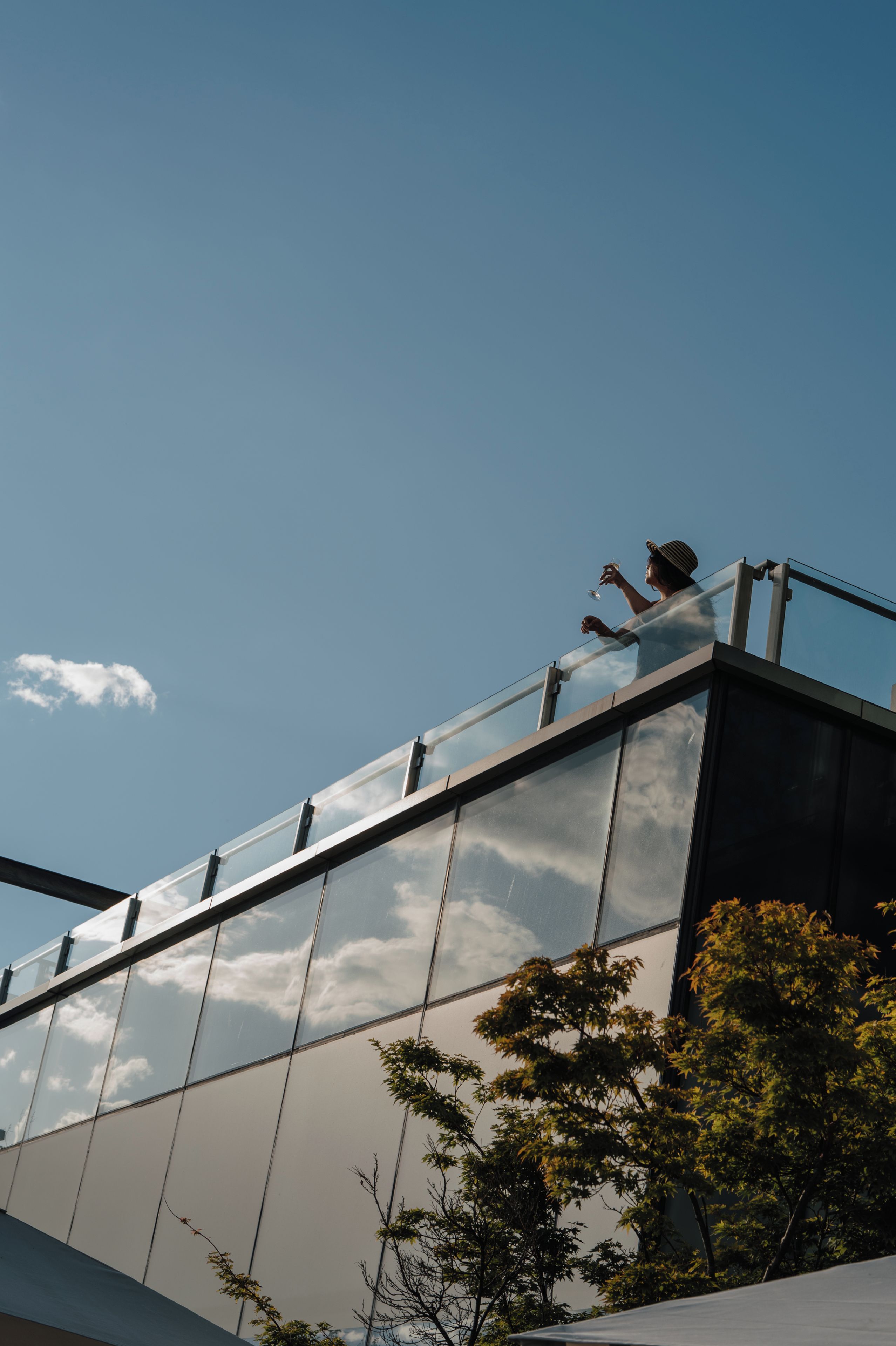 A modern building with a glass facade reflecting the sky and clouds.