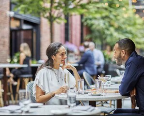 Guests can dine al fresco in this urban setting, surrounded by lush greenery and brick walls.