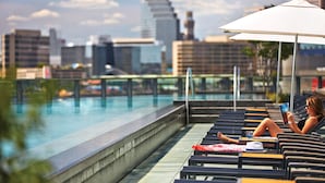 A poolside area with lounge chairs, a person reading a book, and a cityscape in the background. - Four Seasons Hotel Baltimore (Baltimore)