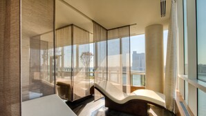 A modern hotel room with a large window, a curved white sofa, and a view of the city. - Four Seasons Hotel Baltimore (Baltimore)