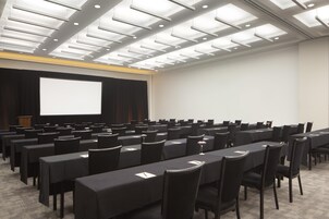 Un salón de conferencias con mesas, sillas, una pantalla de proyector y un atril.