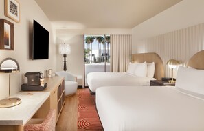 A hotel room with a bed, a desk with a lamp, a coffee maker, and a TV.