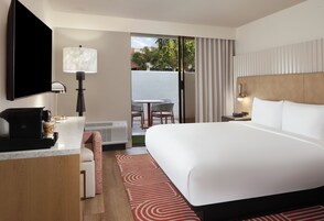 Habitación de hotel con cama, escritorio con cafetera, televisor, lámpara, silla y vista al exterior.