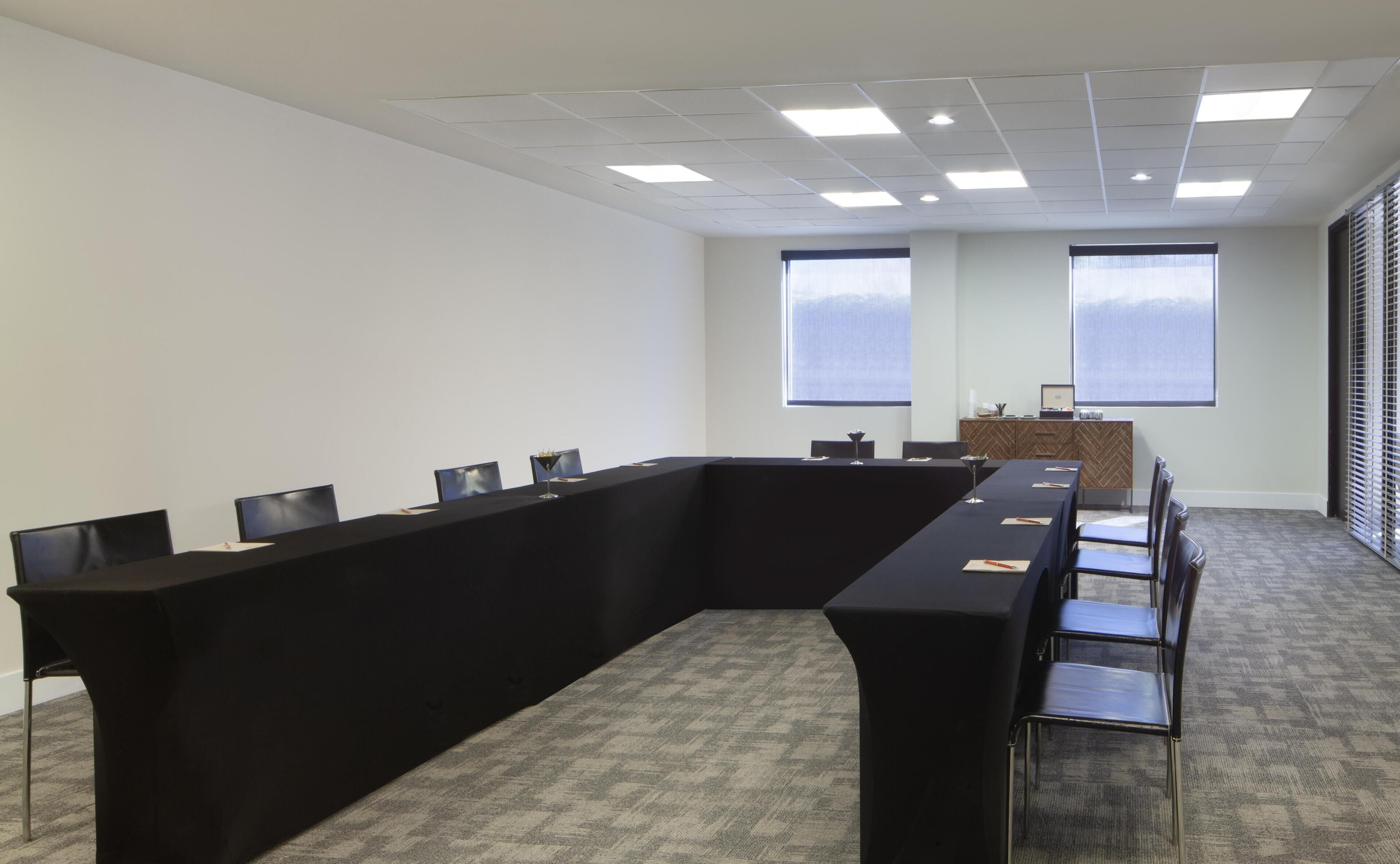 Un salón de conferencias con una larga mesa, sillas, un armario y dos ventanas.