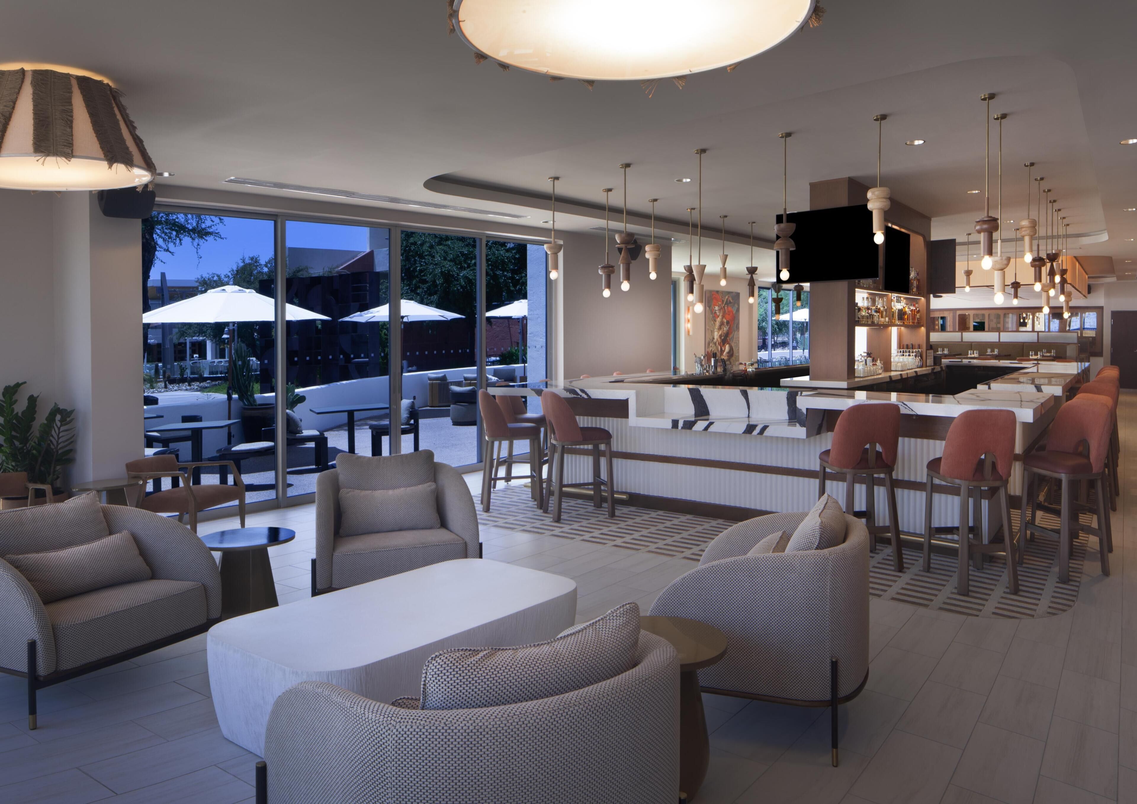 A modern lounge area with seating, a bar, and large windows offering views of the outdoors.