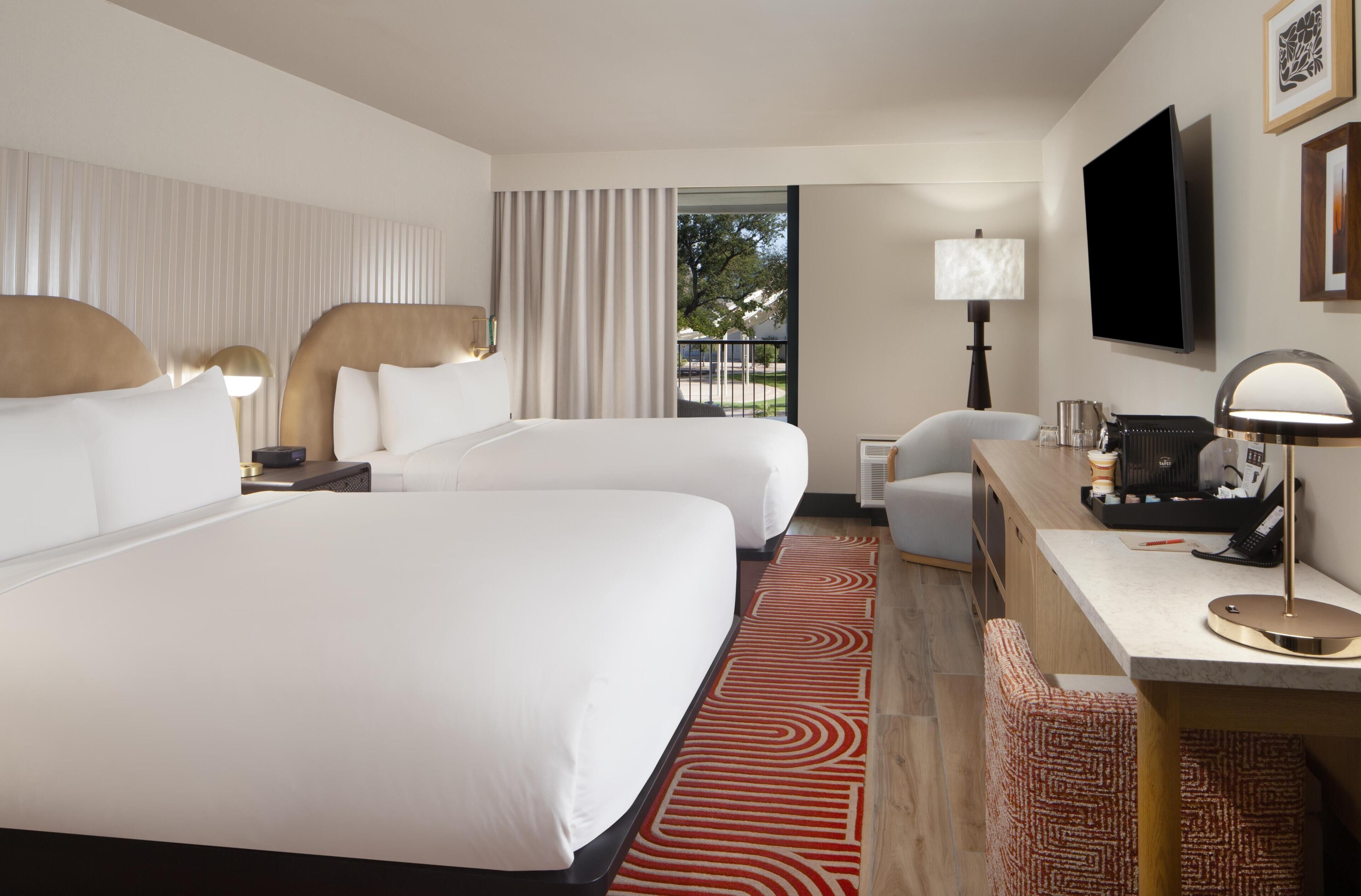 A hotel room with two beds, a desk, a chair, a TV, and a window with a view.