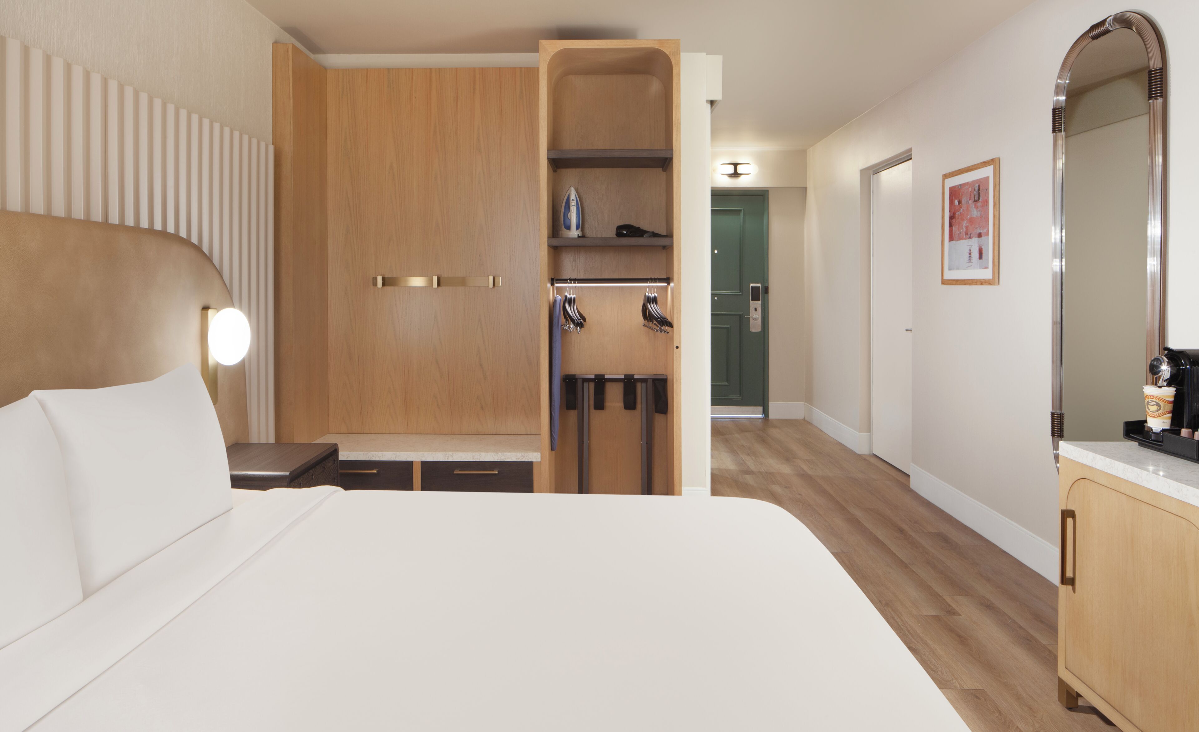 A hotel room with a bed, a wardrobe, a mirror, and a coffee machine.