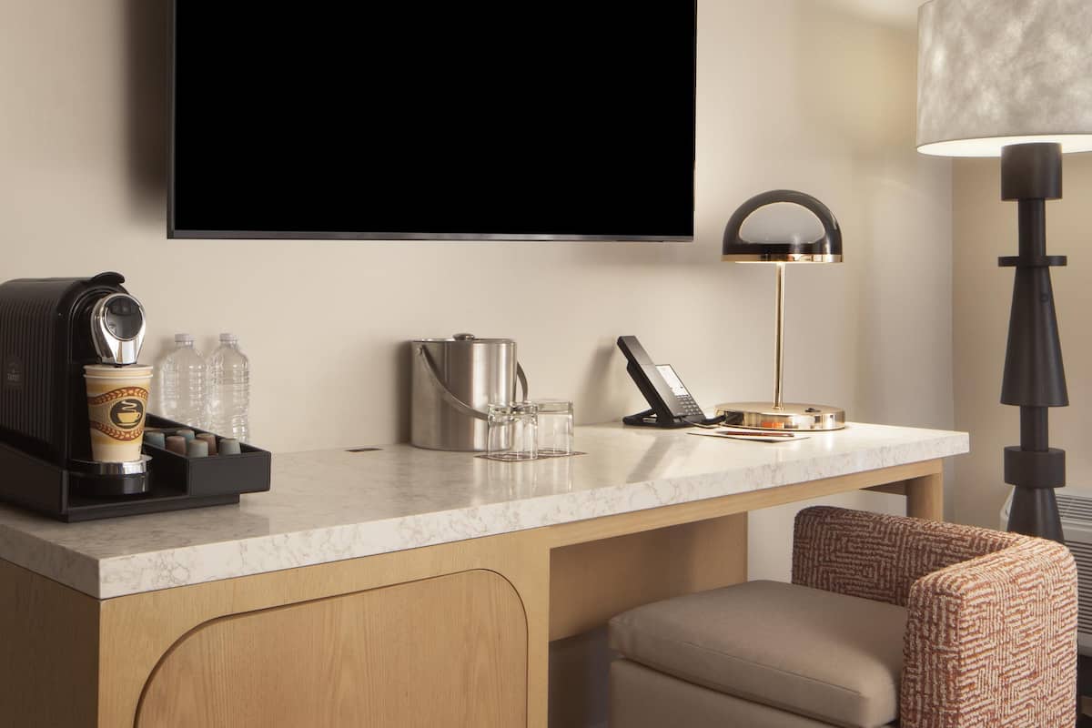A hotel room with a marble countertop, a coffee machine, a kettle, a telephone, a lamp, and a sofa.