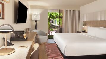 A hotel room with a bed, desk, chair, TV, and a view of the outdoors.