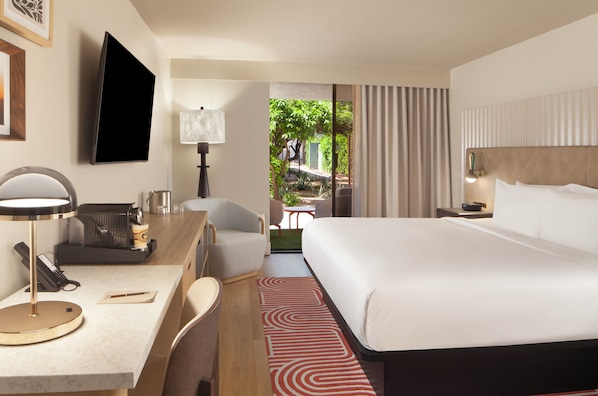 Habitación de hotel con cama, escritorio, silla, televisión y vistas al exterior.