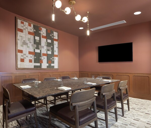 A conference room with a large table, chairs, a flat-screen TV, and a decorative wall piece.