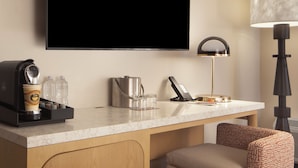 Camera d'albergo con un top in marmo, una macchina per caffè, un bollitore, un bicchiere, un telefono e una lampada.