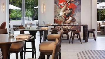 A restaurant with round tables, cushioned chairs, and a large painting on the wall.
