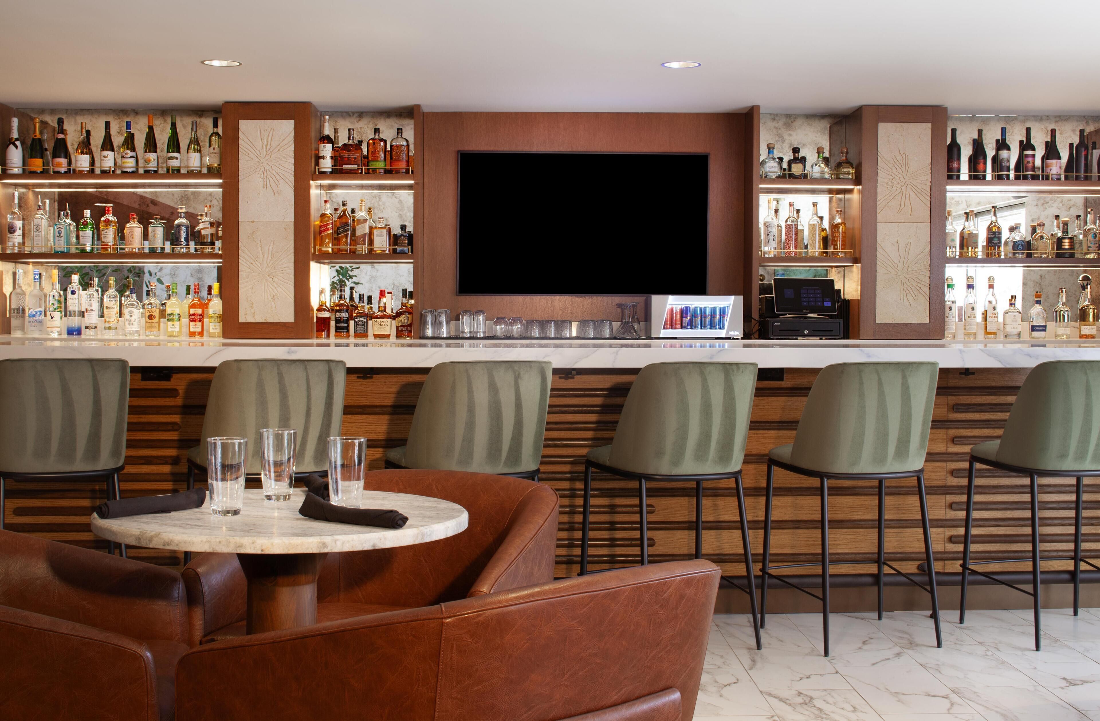 Zona de bar con un televisor de pantalla plana, taburetes y una variedad de botellas de licor.