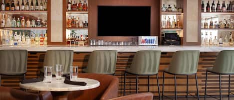 Zona de bar con un televisor de pantalla plana, taburetes y una variedad de botellas de licor.