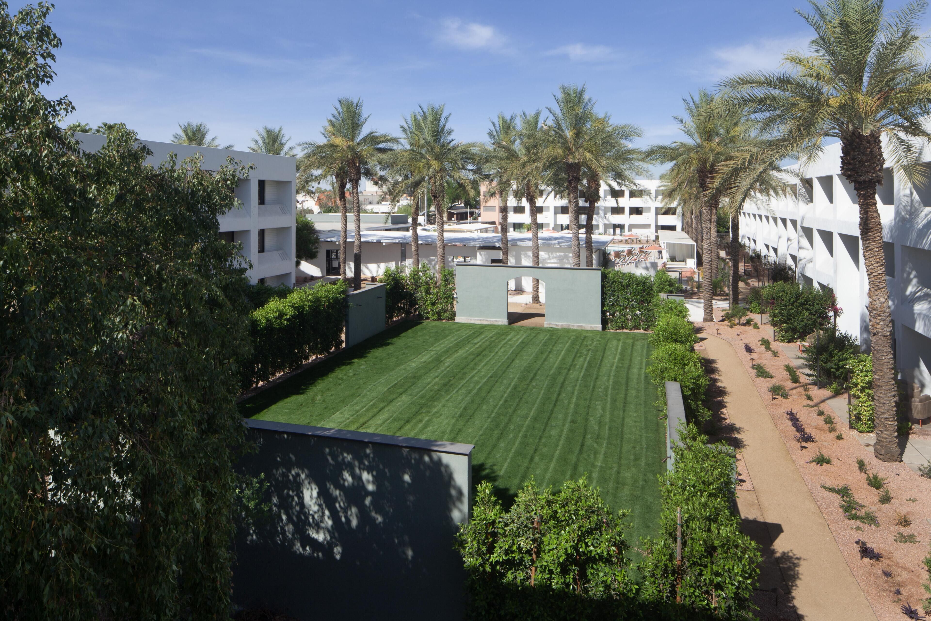 A courtyard with a green lawn, palm trees, and a building with balconies.