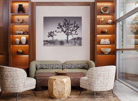 A modern living room with a sofa, two armchairs, a coffee table, and a wall-mounted shelf with decorative items.