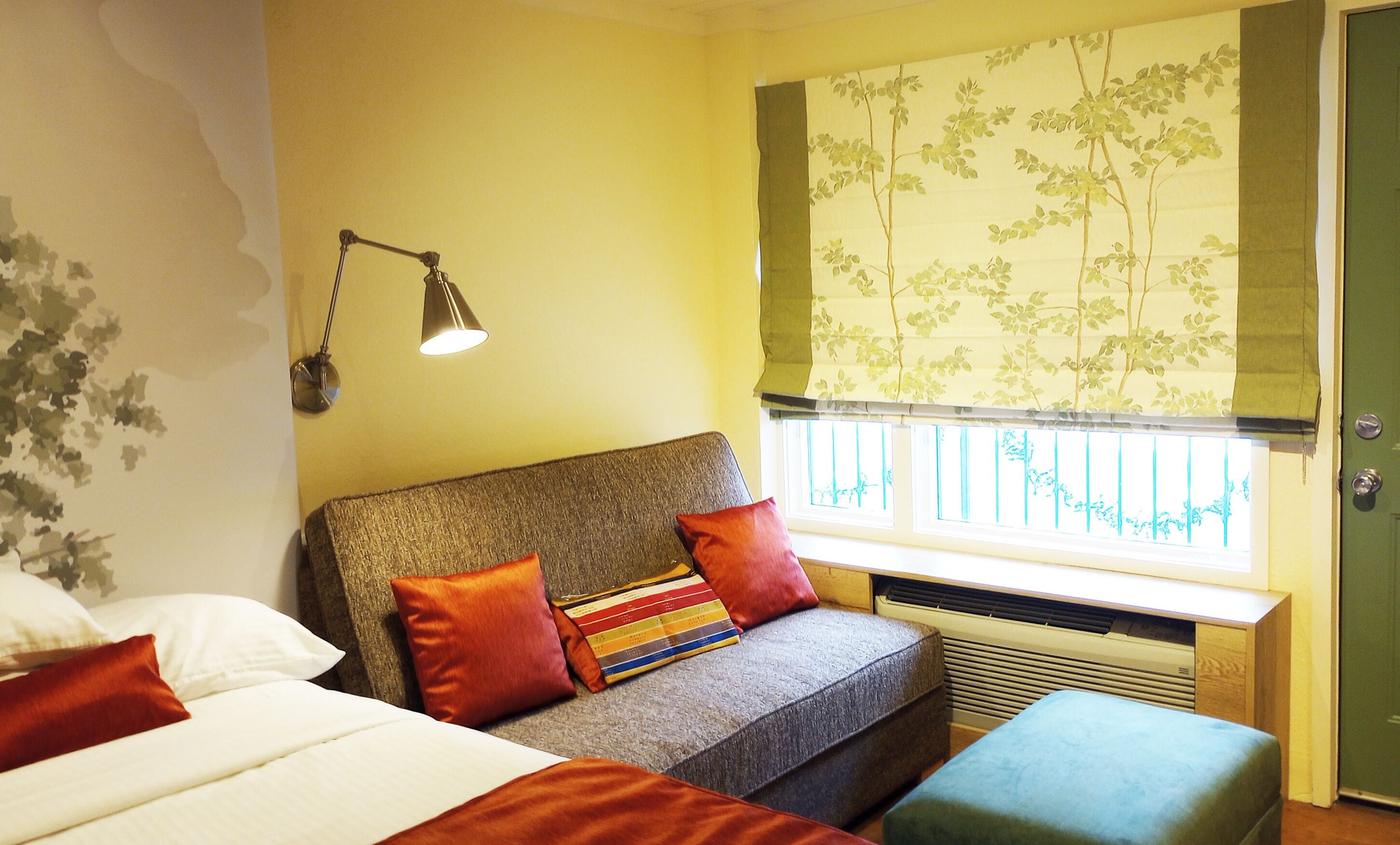 A bedroom with a bed, a sofa, a window with a view, and a lamp.