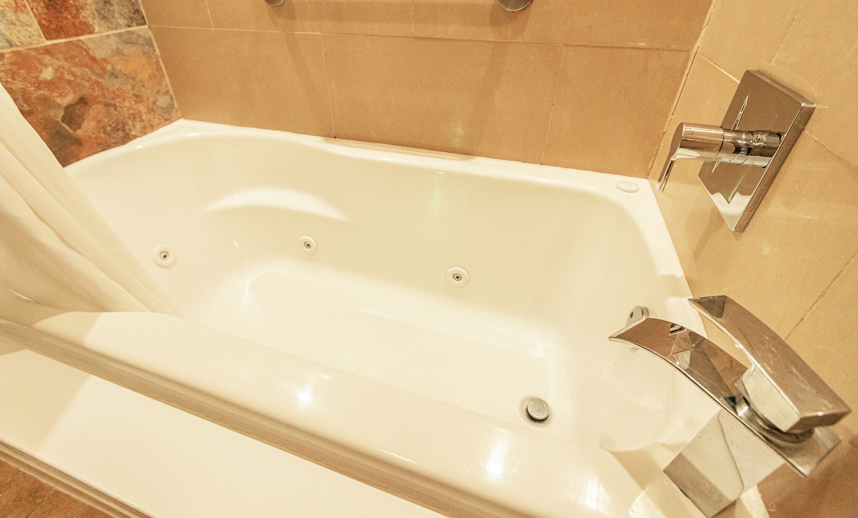 A modern bathroom with a white bathtub, chrome fixtures, and a tiled wall.