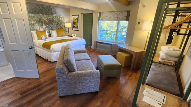 Quarto com cama, sofá, escrivaninha e janela com vista para árvores.