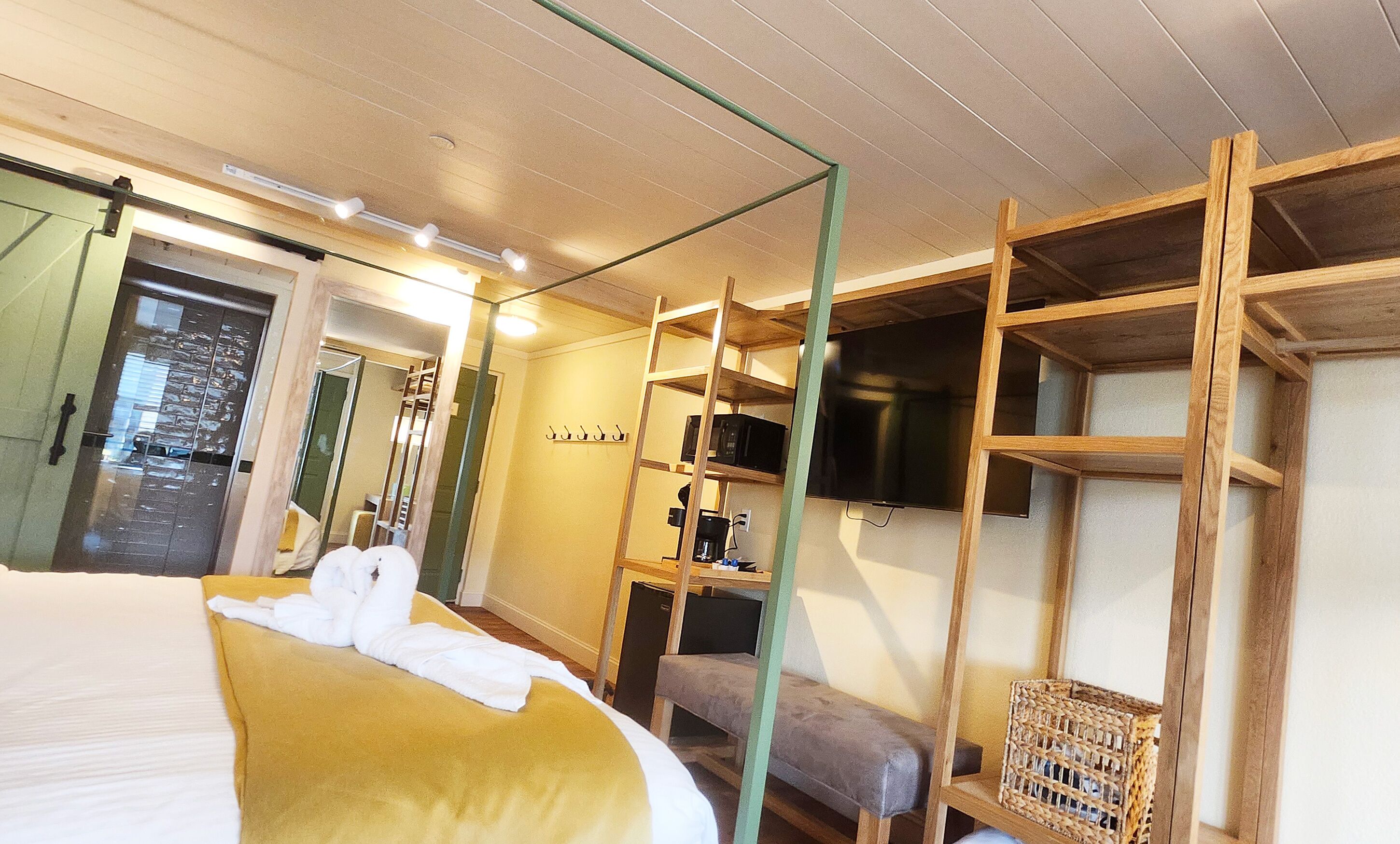 A hotel room with a bed, a wooden shelf unit, a television, and a small seating area.
