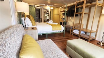 Ein Hotelzimmer mit Bett, einer Couch, einer Bank und einem Fernseher an der Wand.