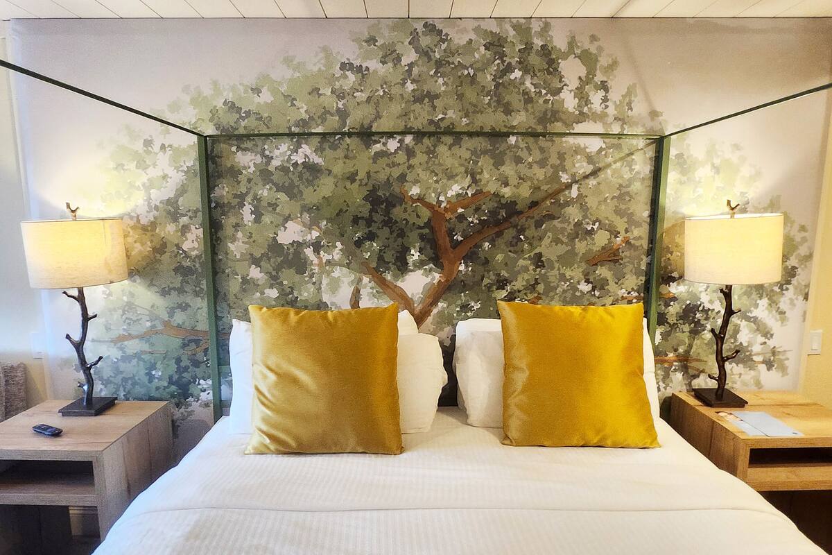A bed with a canopy, two lamps on either side, and a tree mural on the wall behind.