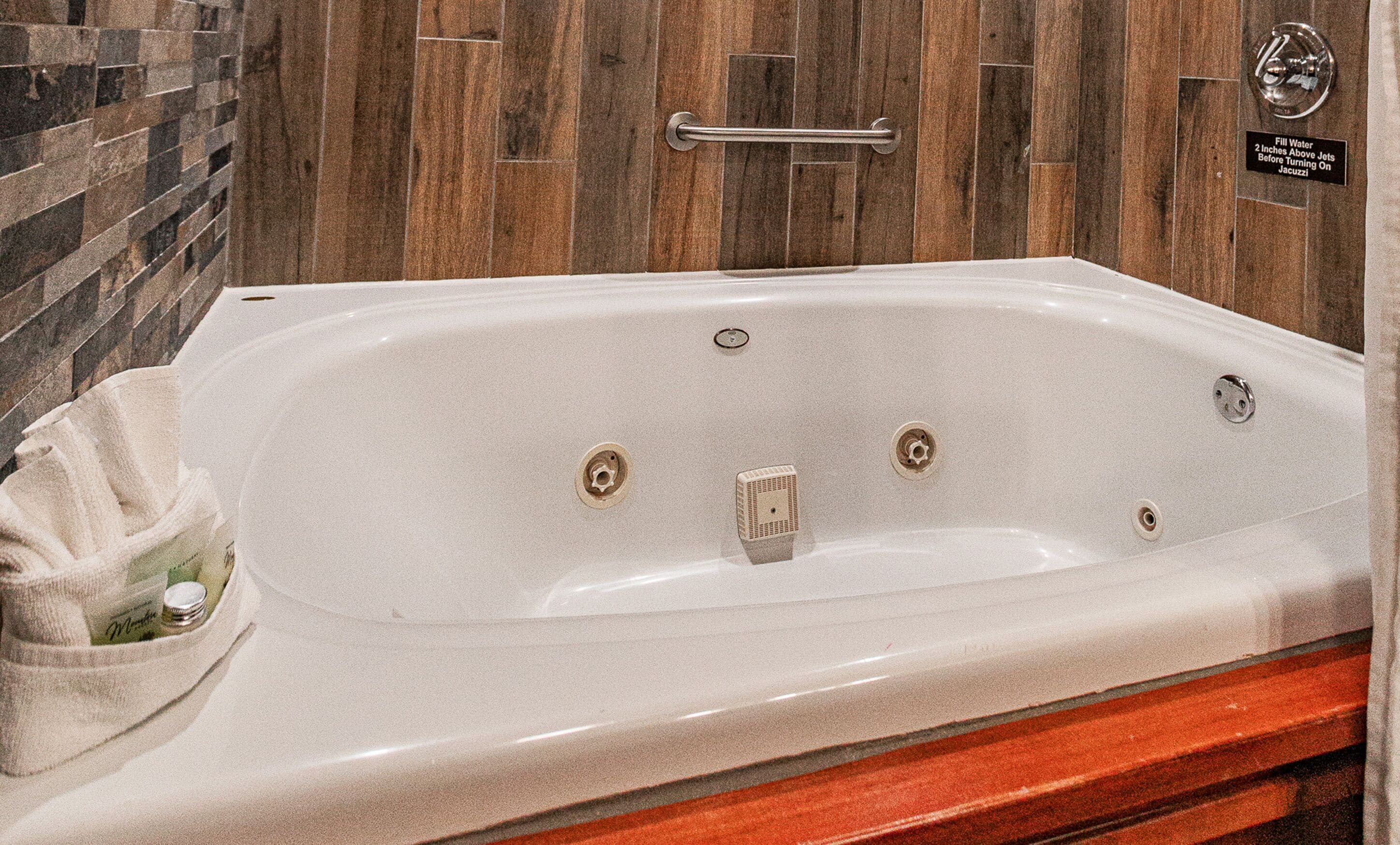 Una bañera blanca con un banco de madera, una toalla y un grifo.