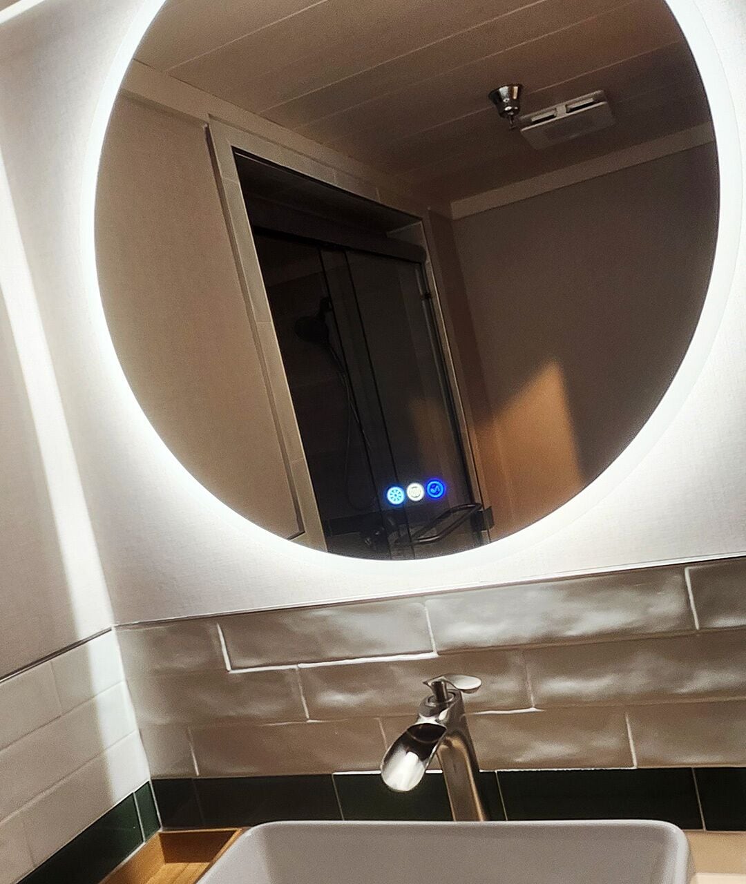 Une salle de bain avec un miroir rond, un lavabo et un espace douche.