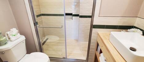 Un baño con ducha de vidrio, inodoro y lavamanos con tocador de madera.