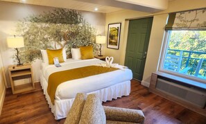 A neatly arranged bedroom with a bed, bedside tables, a window with a view, and a green door. - Arbors at Island Landing Hotel & Suites (Pigeon Forge)