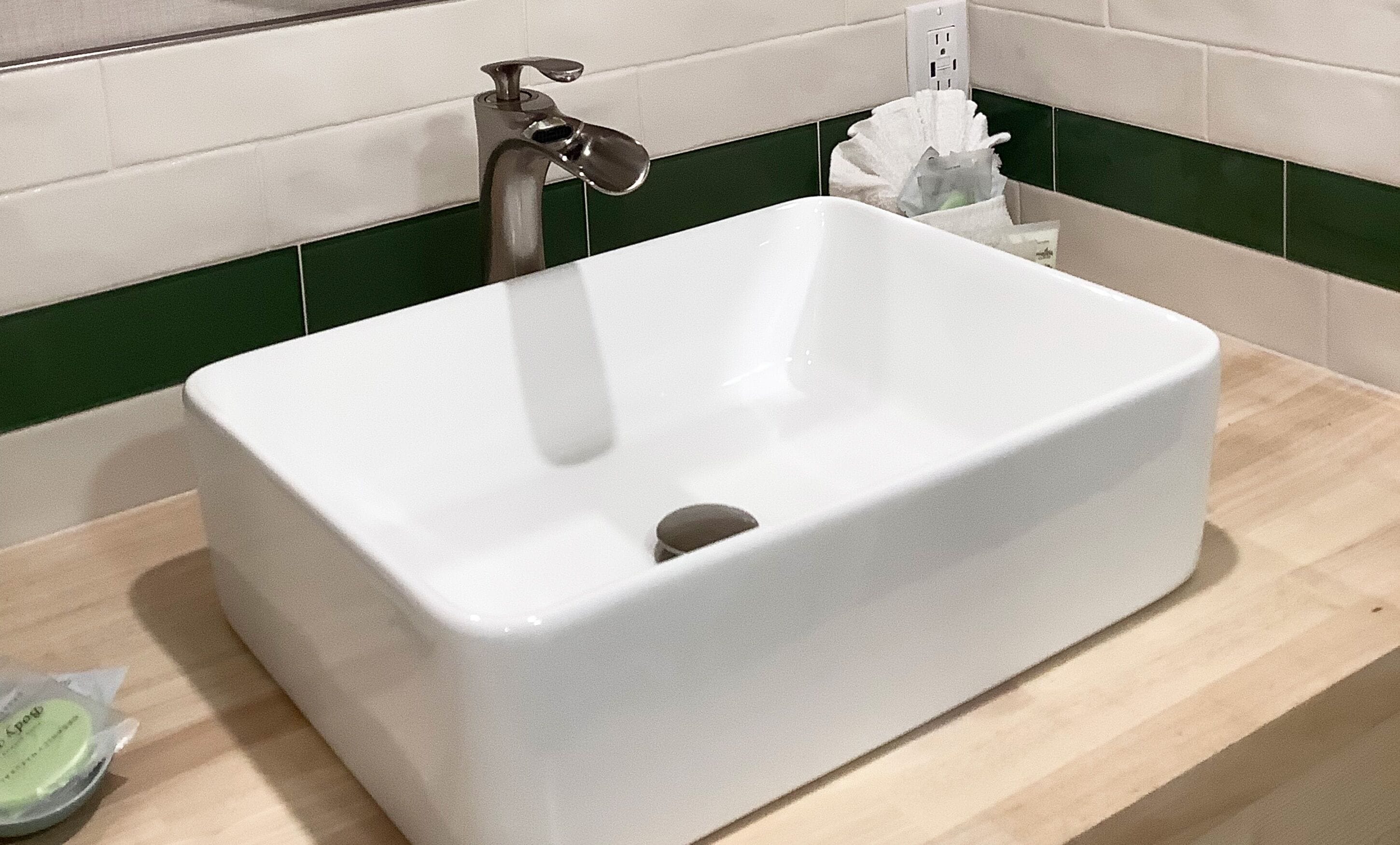 A white rectangular sink with a single faucet, a tissue dispenser, and a small bottle on a wooden countertop.
