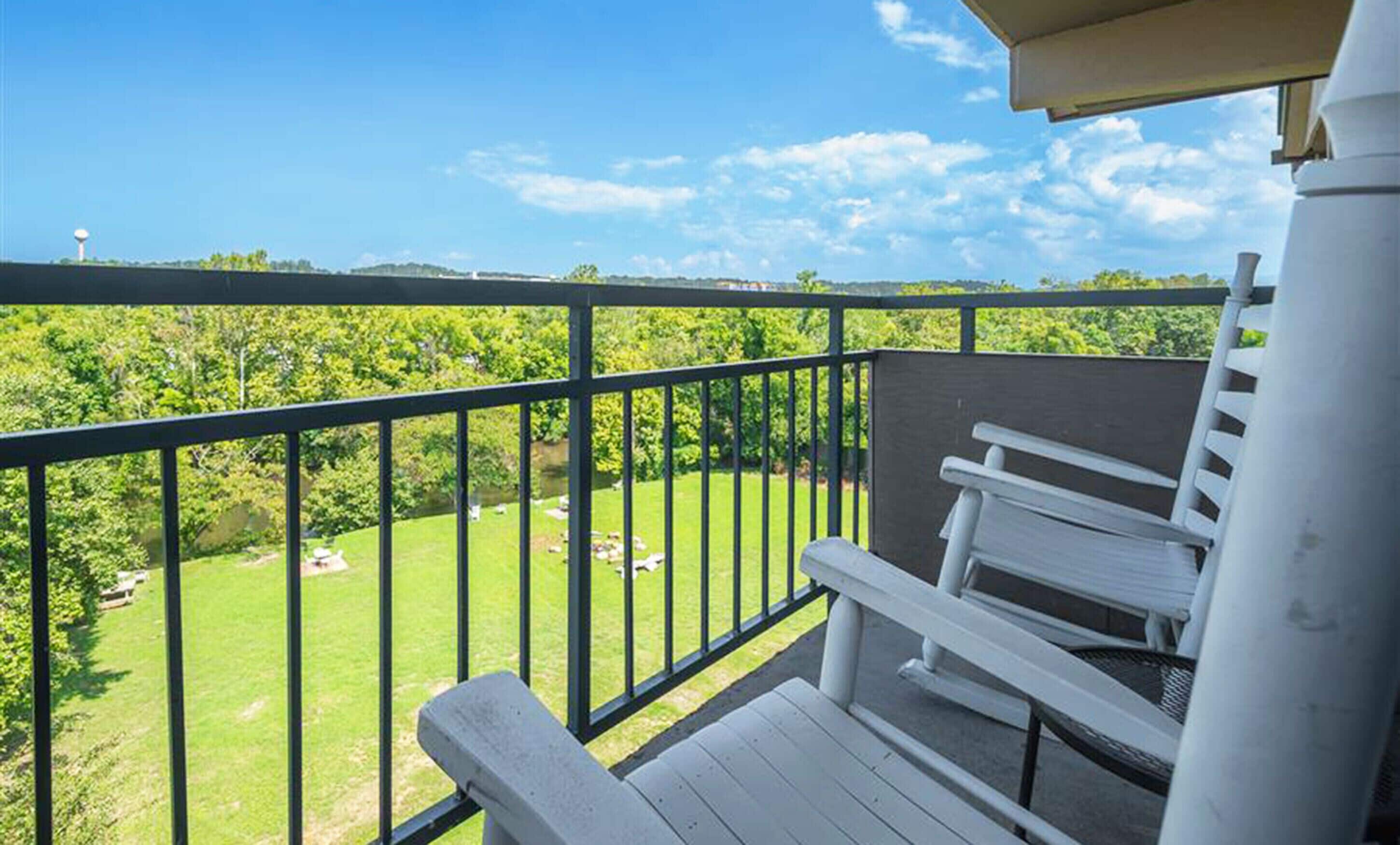 Een balkon met uitzicht op een groen landschap, een witte bank en een watertoren in de verte.