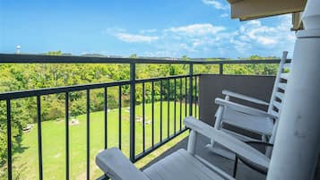A balcony with a view of a green landscape, a white bench, and a water tower in the distance.