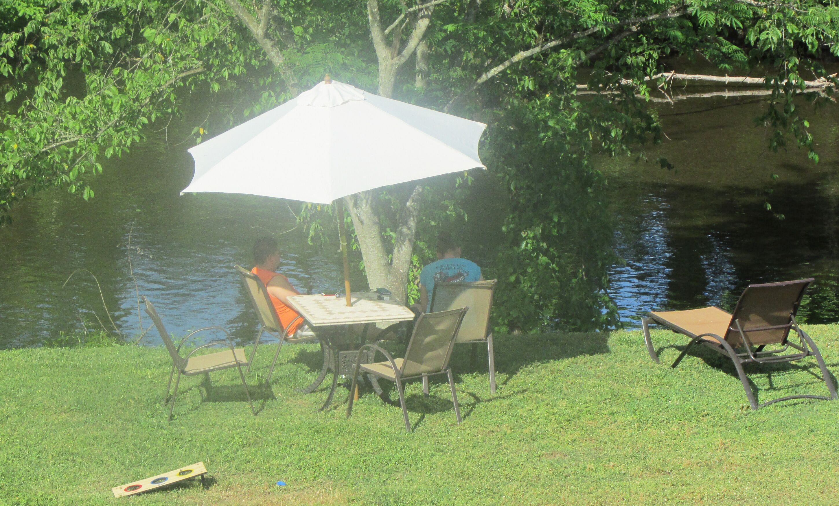 Un área de comedor al aire libre con una mesa y sillas bajo un paraguas grande, con vista a una masa de agua.