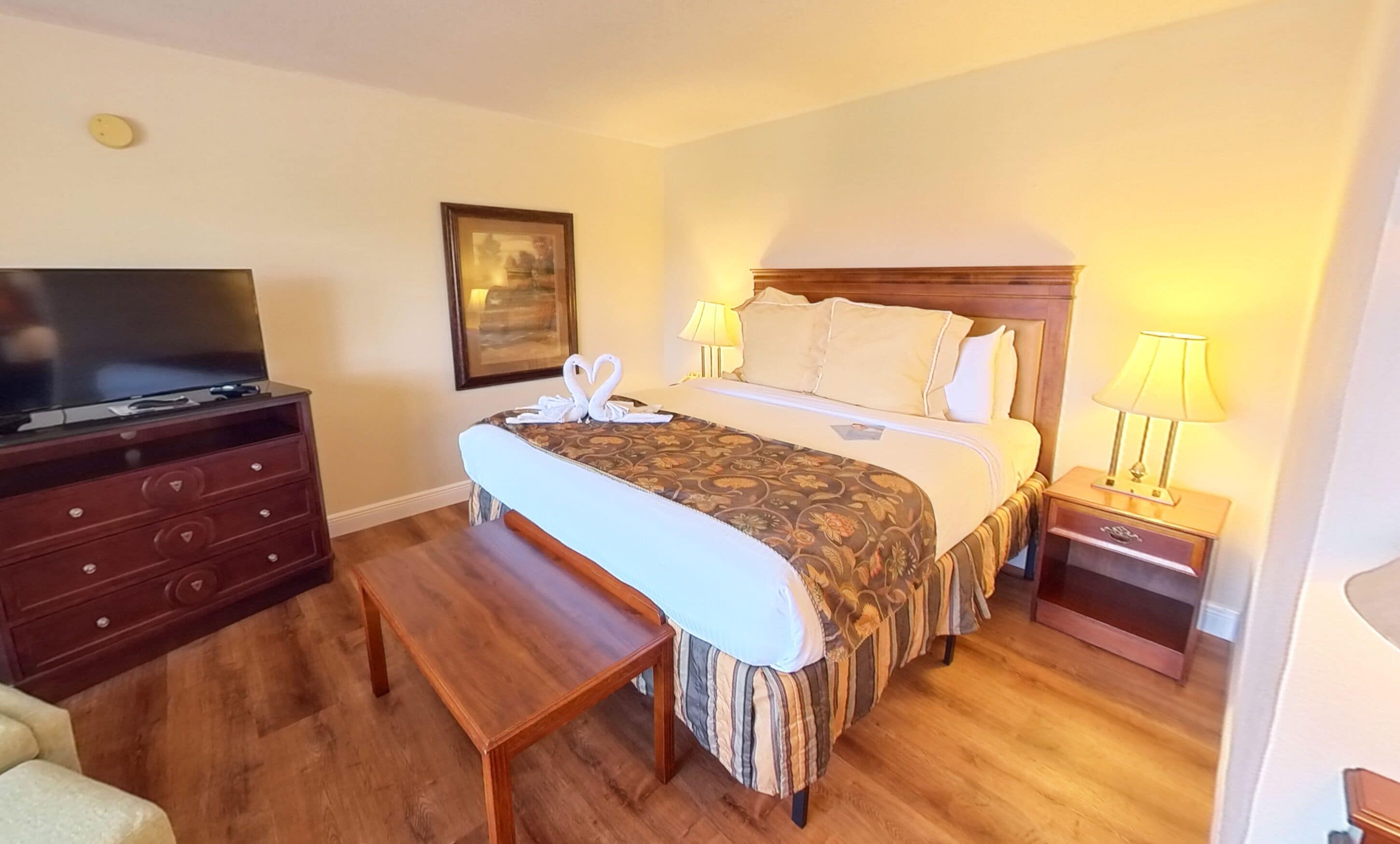 Ein Hotelzimmer mit Bett, Nachttischlampen, Fernseher, einem hölzernen Schminktisch und einer Bank.
